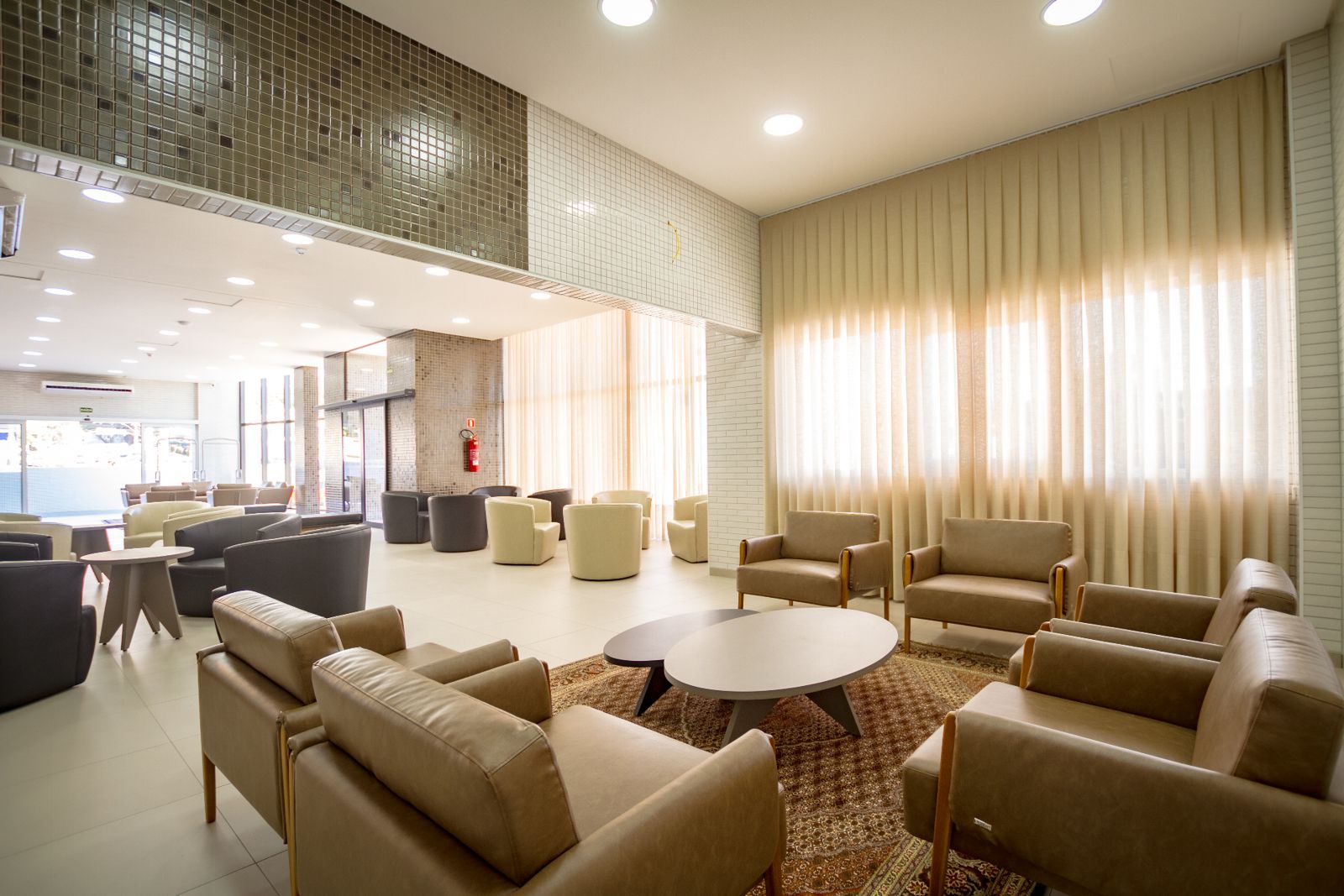 Lounge do lobby com sofás, mesa de centro e cortinas claras — Hotel Confiance Barigui