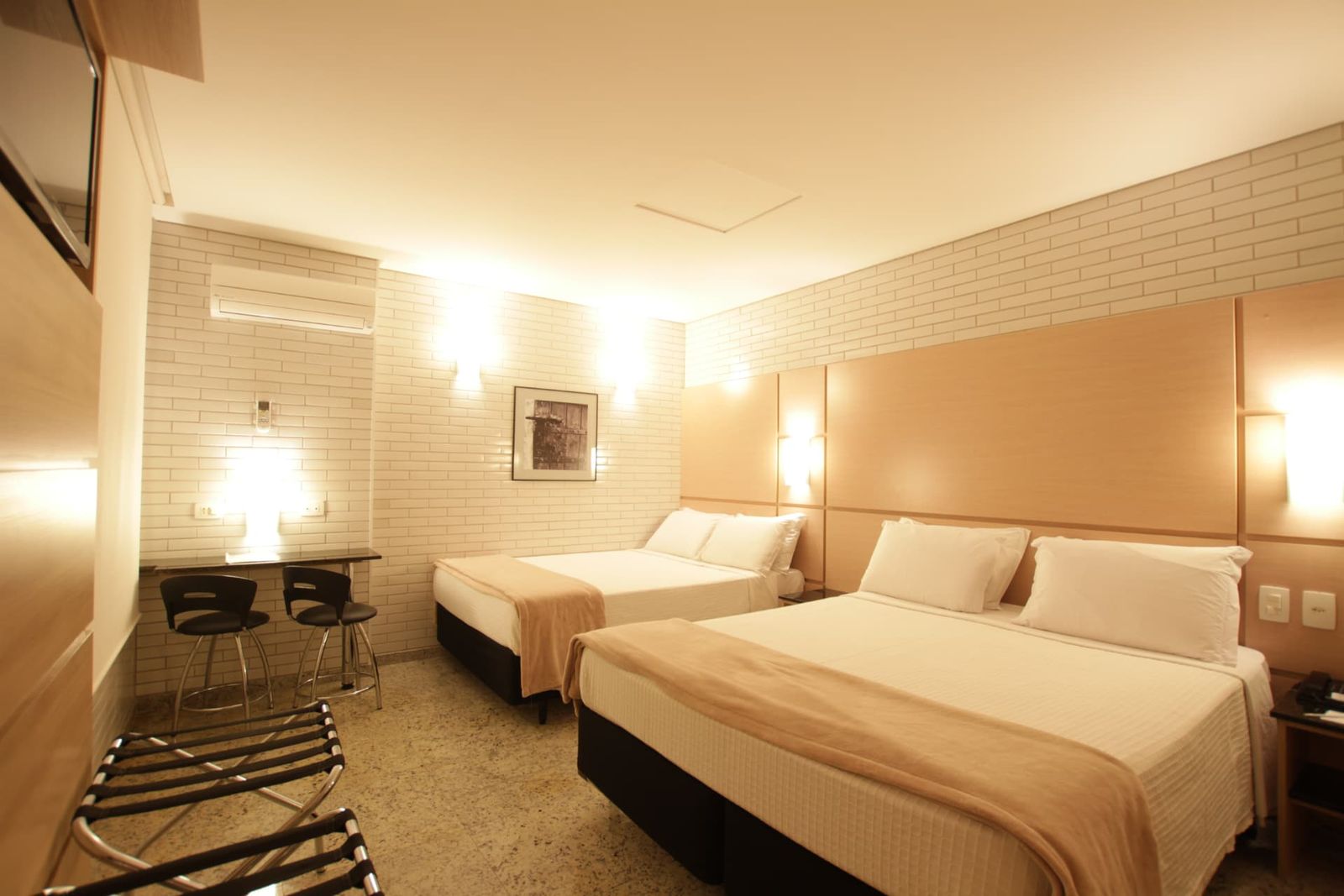Apartamento Standard Quádruplo Casal Twin com duas camas de casal, escrivaninha e parede de tijolinho branco — Hotel Confiance Centro Cívico